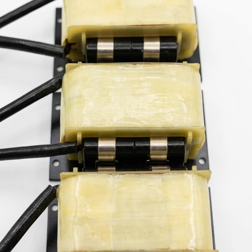 A row of varnished transformers on a mounting rail, lead terminated